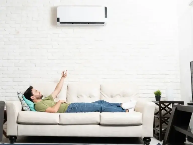 Man on couch adjusting a ductless mini split heat pump with the remote control.